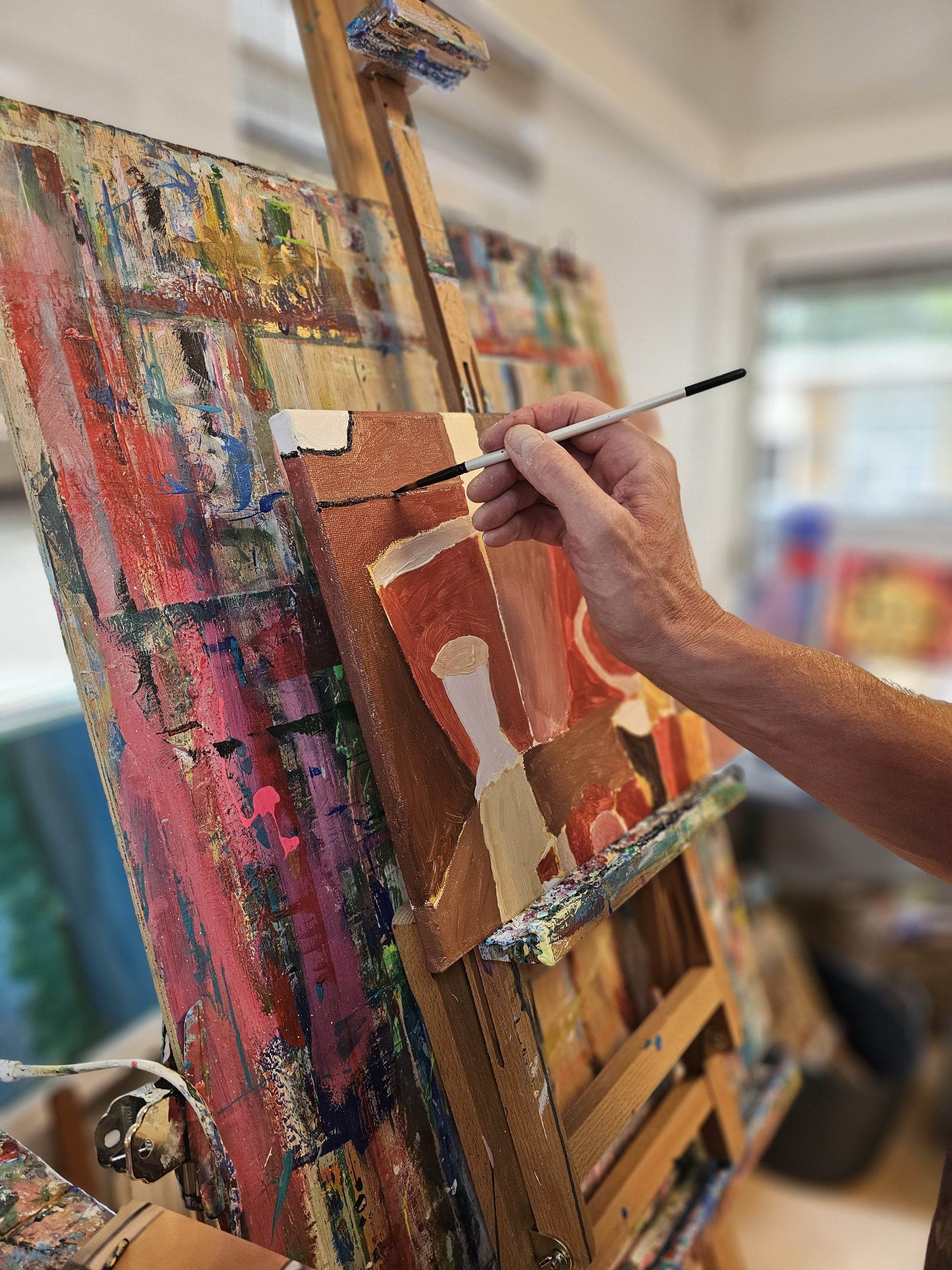 Deelnemer schildert tijdens een schilderworkshop zonder ervaring met penseel aan een kleurrijk doek op een ezel in het atelier