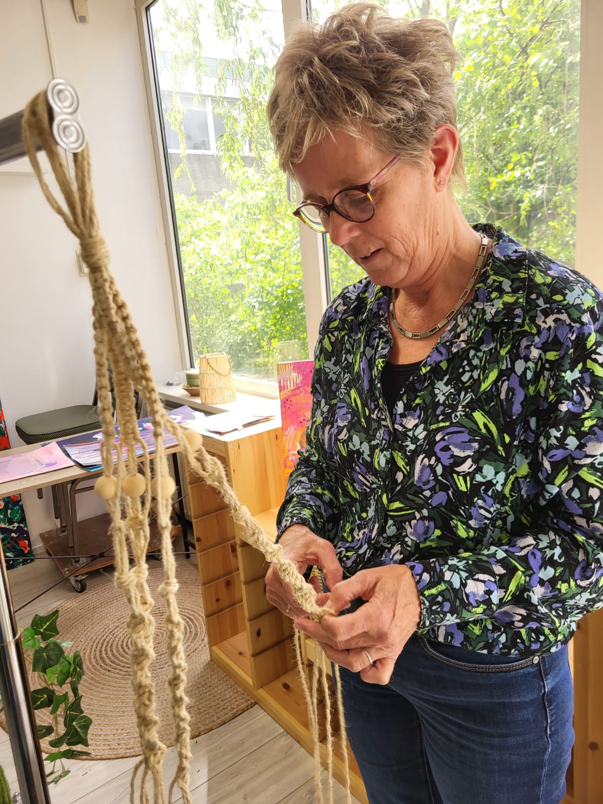 Deelneemster knoopt tijdens de macramé workshop een plantenhanger van touw met houten kralen