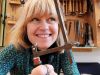 Docent Sacha Ofman houdt lachend een figuurzaag omhoog in haar edelsmeedatelier vol gereedschap